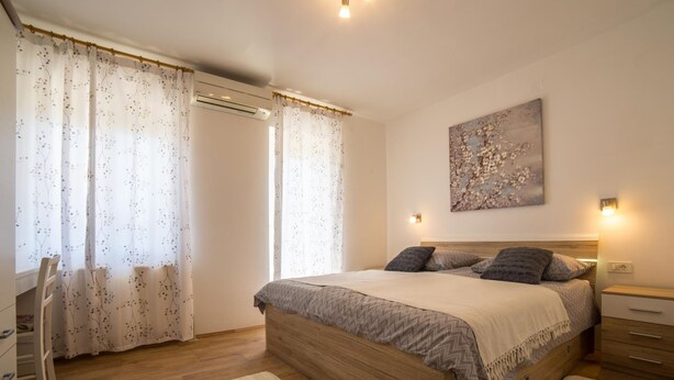 A bedroom with a wooden bed, two bedside tables, a wall-mounted light, and a floral painting. - Apartment Raspolic no.2 by Interhome (Opatija/Kastav)