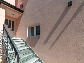 Eine Treppe führt zu einer Tür mit einem Fenster, einem Metallgeländer und einer strukturierten Wand.