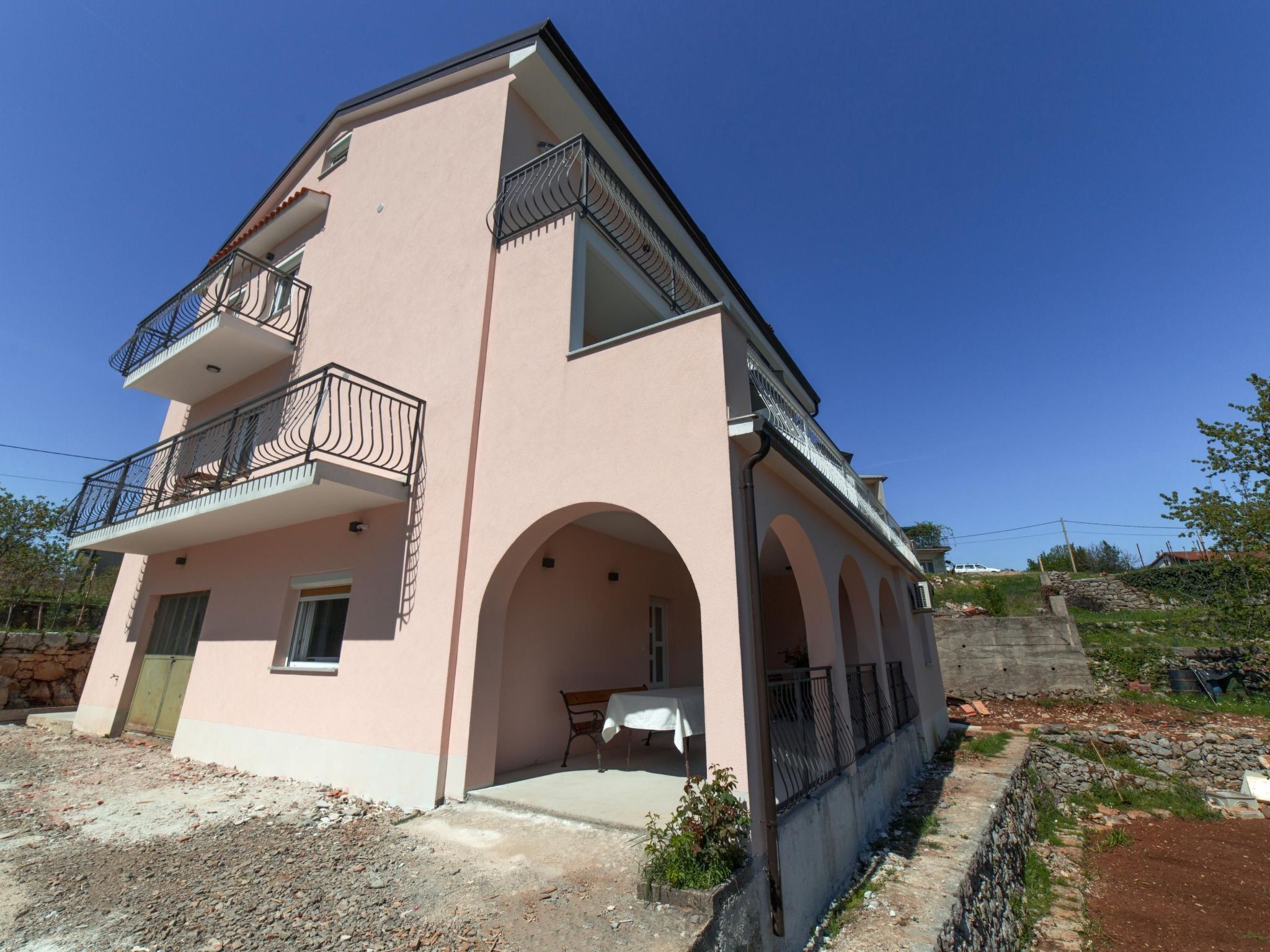 A two-story building with a pink facade, a balcony with metal railings, and an arched entrance.