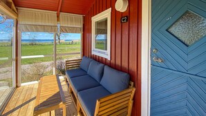 Een houten terras met een bank en tafel, een blauwe deur en een raam met uitzicht op de omgeving.