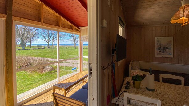 Een houten chalet met een schuifglasdeur naar een terras, een tafel met stoelen, en een televisie aan de muur.