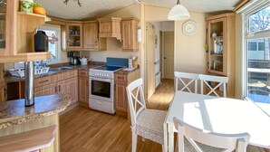 A compact kitchen with wooden cabinets, a stove, and a dining area with white chairs. - 2 bedroom beautiful home in Färjestaden (Färjestaden)
