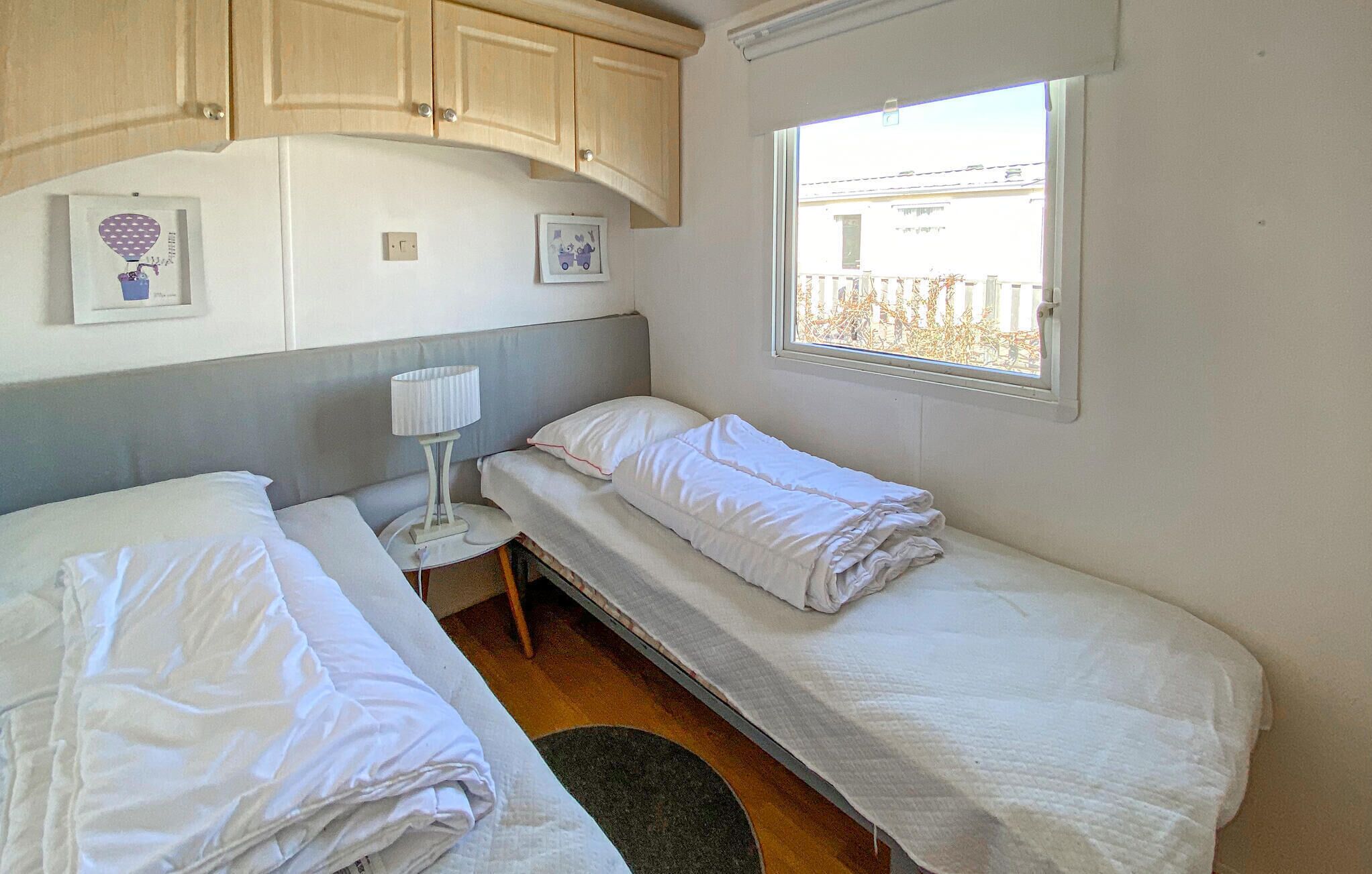 A room with two beds, a small table with a lamp, wooden cabinets, and a window with a view.