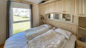 A bedroom with a large bed, a window with curtains, a mirror above the bed, and a small bedside table. - 2 bedroom beautiful home in Färjestaden (Färjestaden)