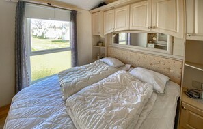 Quarto com uma cama grande, janela com cortinas, espelho sobre a cama e uma pequena mesa de cabeceira.