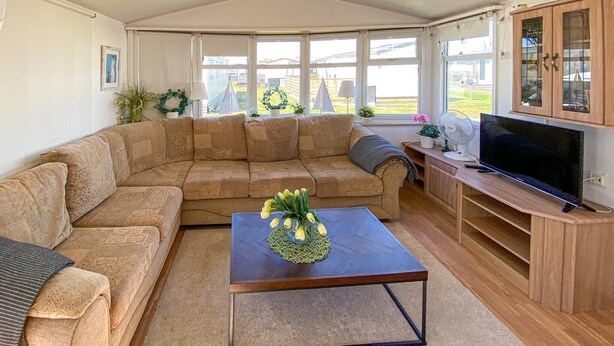 A living room with a sectional sofa, a coffee table with flowers, a television, and a view of the outside. - 2 bedroom beautiful home in Färjestaden (Färjestaden)