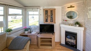 A cozy living room with a fireplace, a television, a wooden cabinet, and a window with a view of the outside. - 2 bedroom beautiful home in Färjestaden (Färjestaden)
