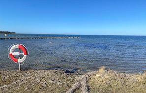 Uma boia salva-vidas numa costa rochosa, com vista clara para a água e um cais ao longe.