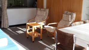 Een knus kamertje met kitchenette, twee gestreepte stoelen, een klein houten tafeltje en een bed met streepjesbeddengoed.