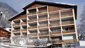 Een hotel met meerdere verdiepingen, balkons, een parkeerplaats en een besneeuwd berglandschap.