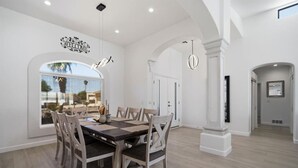 Un comedor amplio con una mesa grande y sillas, un letrero decorativo en la pared y vistas a través de un ventanal.
