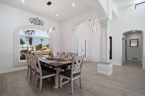 A spacious dining area with a large table and chairs, a decorative wall sign, and a view through a large window. - Donner Delight - Pool, Game Room, Newly Remodeled (Lake Havasu City)