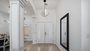 Un pasillo con paredes blancas, suelo de madera, un espejo grande y una lámpara moderna.