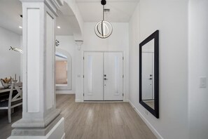 A hallway with white walls, a wooden floor, a large mirror, and a modern light fixture. - Donner Delight - Pool, Game Room, Newly Remodeled (Lake Havasu City)
