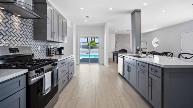 Cocina moderna con una isla grande, estufa y vistas a una piscina a través de puertas de vidrio.