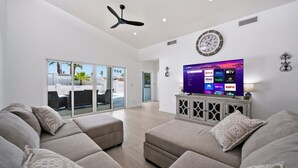 Amplia sala de estar con televisión de pantalla plana, ventilador de techo y un gran ventanal con vistas a un patio.