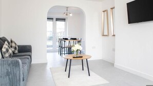 Una sala de estar moderna con un sofá, una mesa de centro redonda y un comedor al fondo.