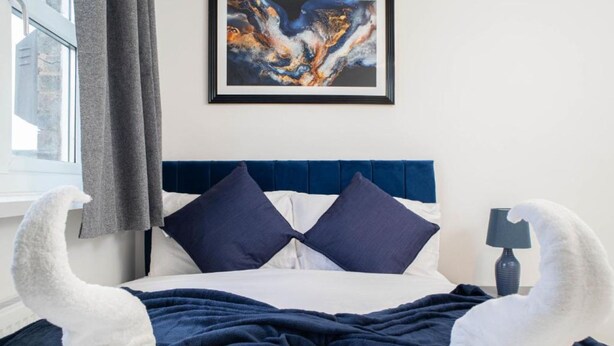 Una cama con cabecera azul, dos almohadas, una colcha y un cuadro abstracto en la pared.