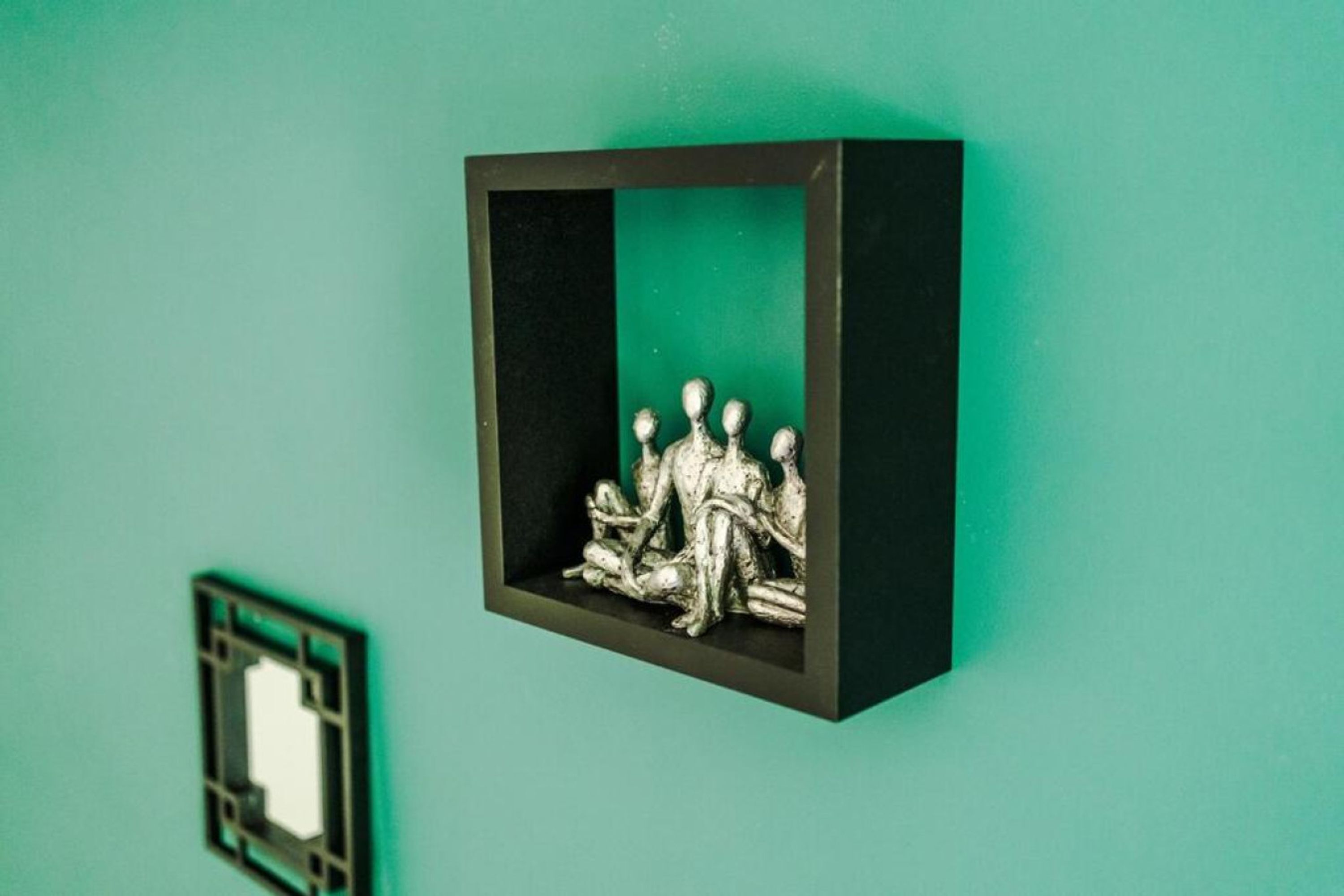A framed sculpture of figures on a teal wall.