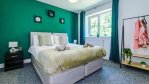 Ein Schlafzimmer mit Bett, Nachttisch, einem Fenster mit Vorhängen und einem Kleiderständer.