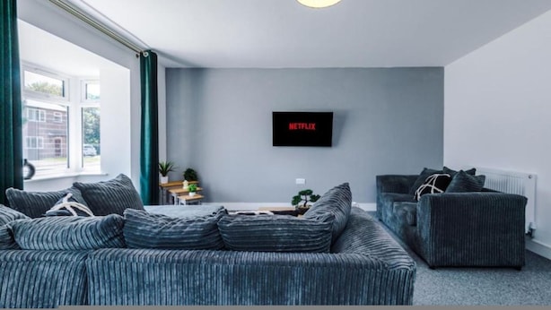 Ein modernes Wohnzimmer mit einem grauen Sofa, einem zusätzlichen Sofa, einem Couchtisch und einem an der Wand befestigten Fernseher.