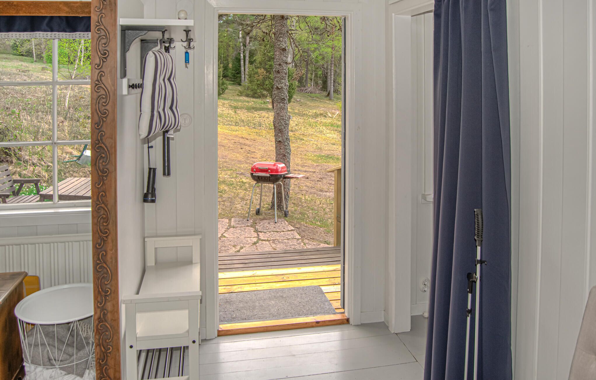 An open door to a deck with a grill, a bench, and a view of a wooded area.