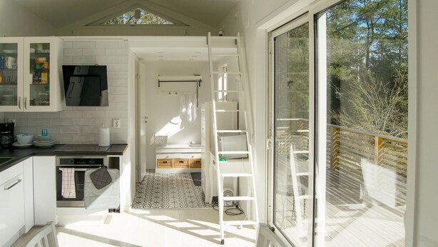 Een compacte keuken met witte kastjes, een eethoek met een tafel en stoelen, en een balkon met houten leuning.