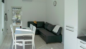 Een ruimtelijk ingerichte leefruimte met een eettafel, een bank, een kitchenette en uitzicht door een deur.