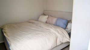 Een enkel bed met een eenvoudig hoofdbord, een neutraal dekleed en enkele kussens.