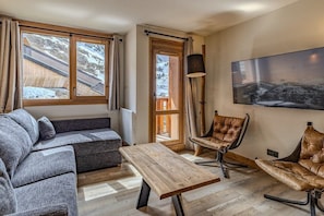 Ein gemütliches Zimmer mit einer Couch, zwei Ledersesseln, einem Holztisch, einem großen Fenster und einem Gemälde an der Wand.