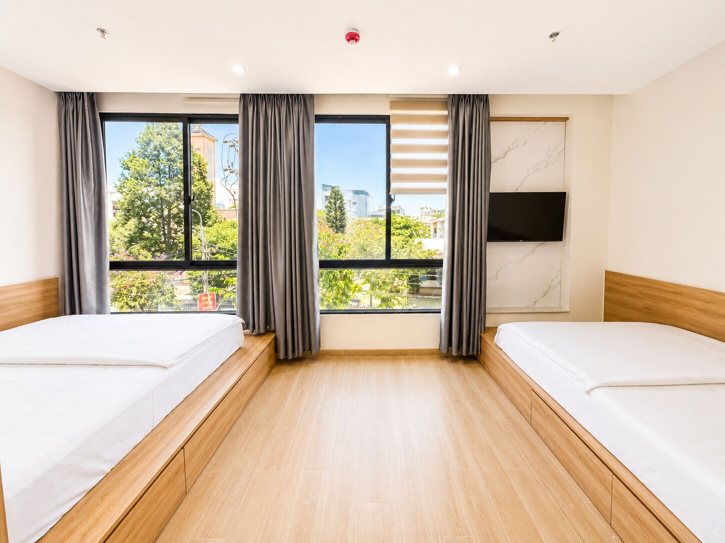 A hotel room with two beds, large windows, a flat-screen TV, and a marble wall.