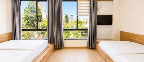 A hotel room with two beds, large windows, a flat-screen TV, and a marble wall.