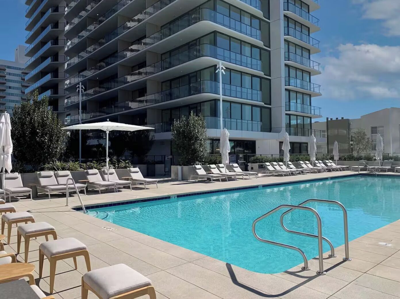 Ett poolområde vid hotellet med solstolar, parasoller och en modern byggnad i bakgrunden.