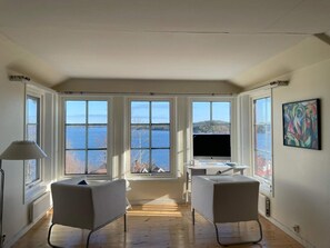 A room with a large window overlooking a body of water, a desk with a computer, two chairs, and a lamp. - 5 Star Holiday Home in Dalaro (Dalaro)