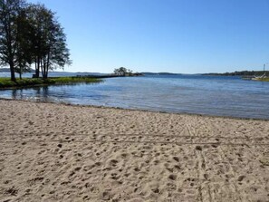 Uma praia arenosa com pegadas que levam a um lago calmo.