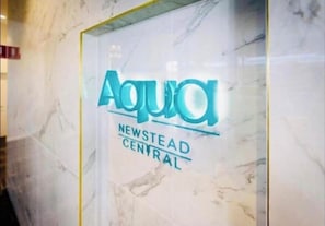 Ein Schild mit dem Logo 'Aqua' und dem Text 'NEWSTEAD CENTRAL' an einer Marmorwand.