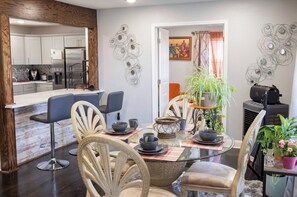 A dining area with a glass table, chairs, and a kitchen in the background.