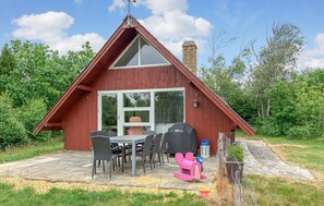 Eine rote Holzhütte mit einer großen Glasdoor, einer Terrasse und Gartenmöbeln sowie einem Schornstein.
