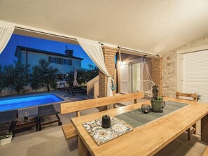 A poolside area with a wooden bench, a table with a decorative tile runner, and a hanging chair. - Villa Javor by Interhome (Pula/Krnica)