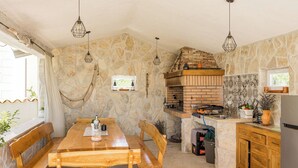 Eine Küche mit Steinwänden, einem Backofen aus Ziegeln, einem Holztisch, Bänken und hängenden Leuchten.