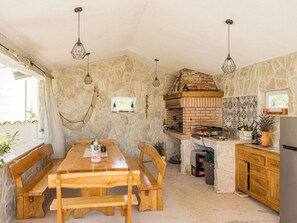A stone-walled kitchen with a brick oven, wooden dining table, benches, and hanging light fixtures. - Villa Javor by Interhome (Pula/Krnica)
