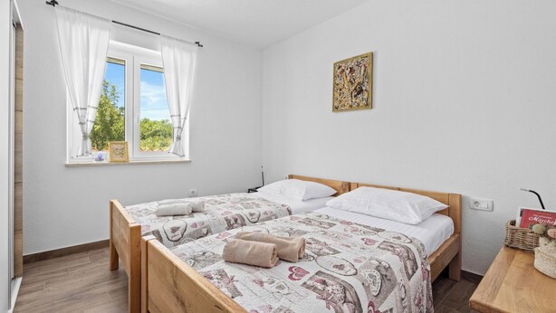 Ein Schlafzimmer mit zwei Holzbetten, einem fenster mit Vorhängen, einem Wandbild und einem Nachttisch mit Korb.