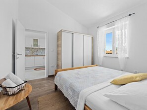 Une chambre à coucher comprenant un lit, une table de chevet en bois, une petite table avec des serviettes, une armoire et une fenêtre avec des rideaux.
