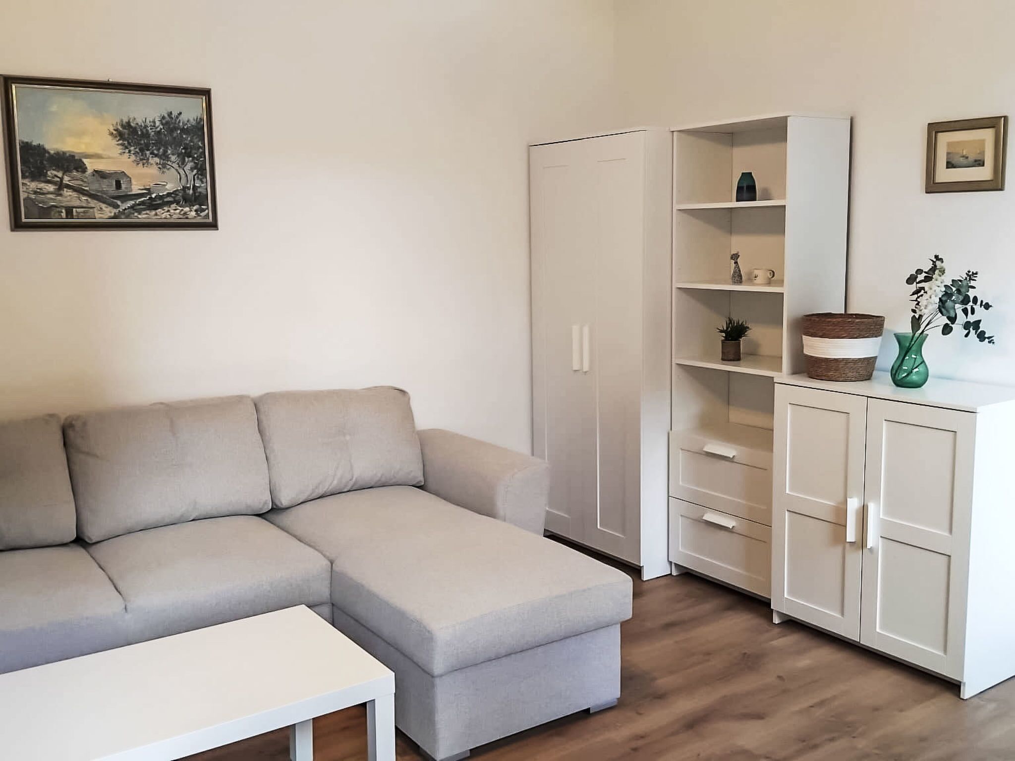 Un salon moderne avec un canapé d’angle beige, une table blanche, une armoire blanche et une étagère ornée d’objets décoratifs.