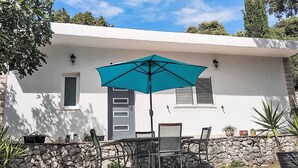 En terrasse med et bord, stole, en søgrøn parasol og krukkeplanter.