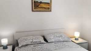 En pænt redt seng med mønstrede puder, et indrammet landskabsmaleri over sengen og sengeborde med lamper på hver side.
