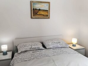 A neatly made bed with patterned pillows, a framed landscape painting above it, and bedside lamps on either side. - mit riesigem Garten by Interhome (Trogir/Seget Donji)