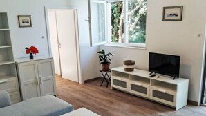En moderne stue med sofa, lille bord, fjernsyn på et hvidt skab og en potteplante.