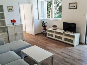 A modern living room with a sofa, a small table, a TV on a white cabinet, and a potted plant. - mit riesigem Garten by Interhome (Trogir/Seget Donji)