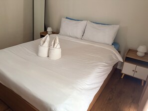 A neatly made bed with white linens, two towels, and a bedside table with a lamp. - Cozy 1-bedroom condo in marvelous Lapu-Lapu with AC (Lapu-Lapu)